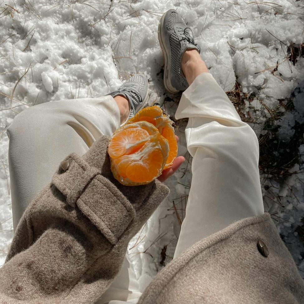 crop woman with tangerine in winter park